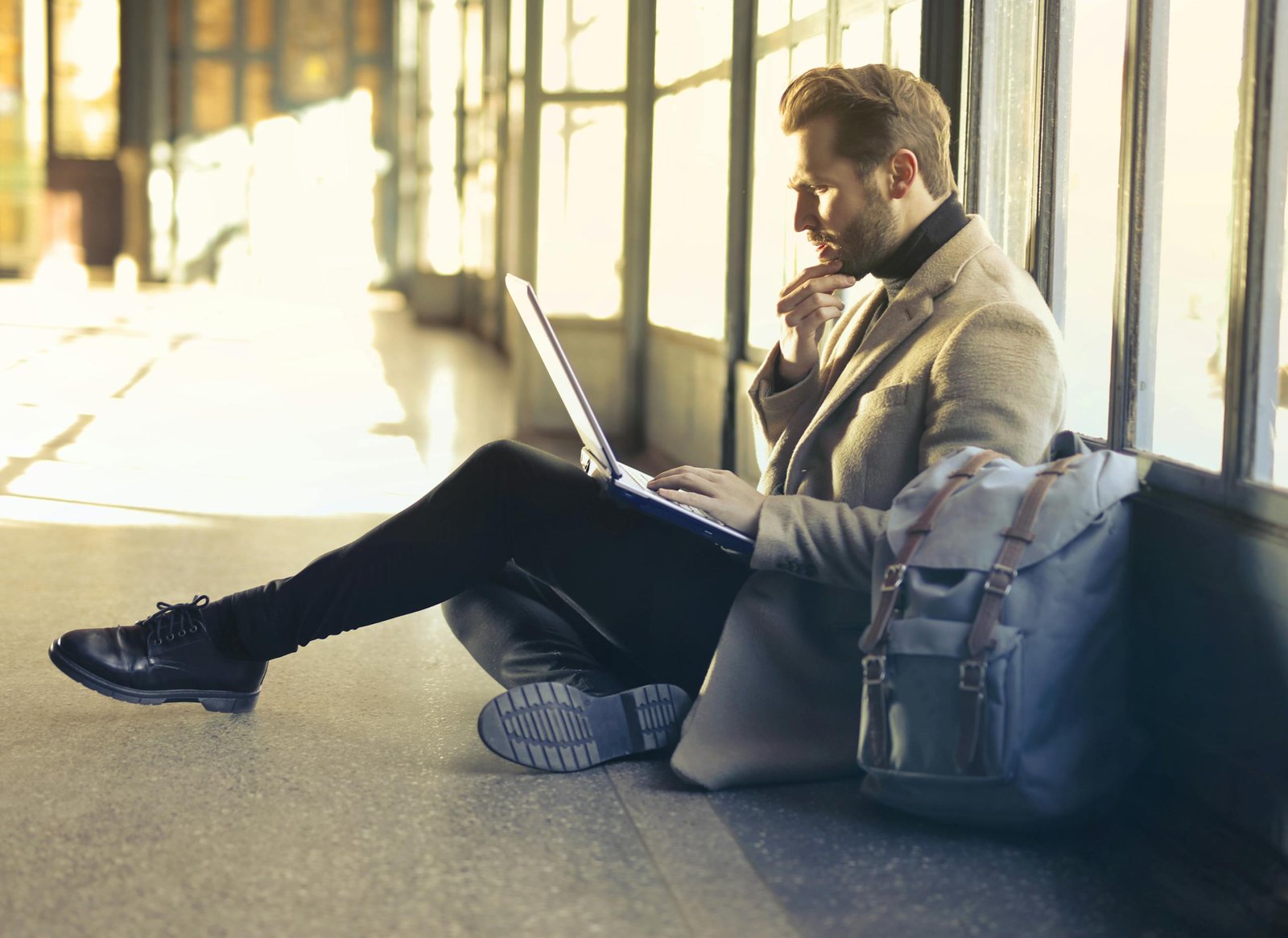 Young man sitting indoors at an airport using laptop. Ideal for remote work themes.