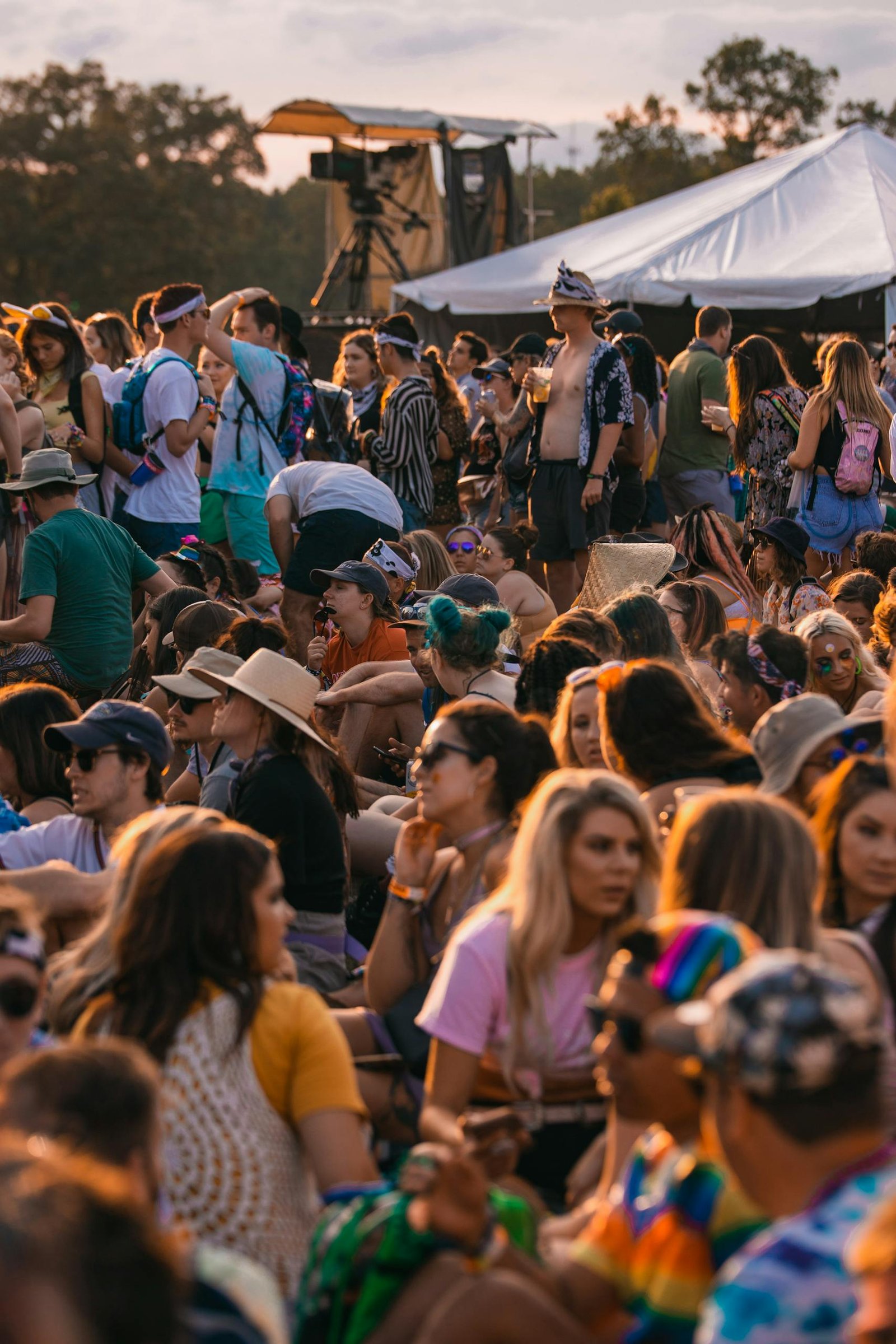 A lively crowd enjoying an outdoor music festival under tents and open skies.